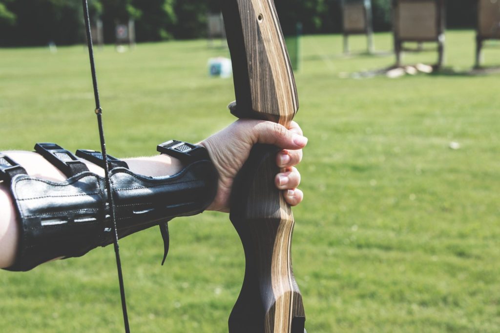 Close-up of an archer's hand holding a bow, ready to aim at targets on a sunny day.